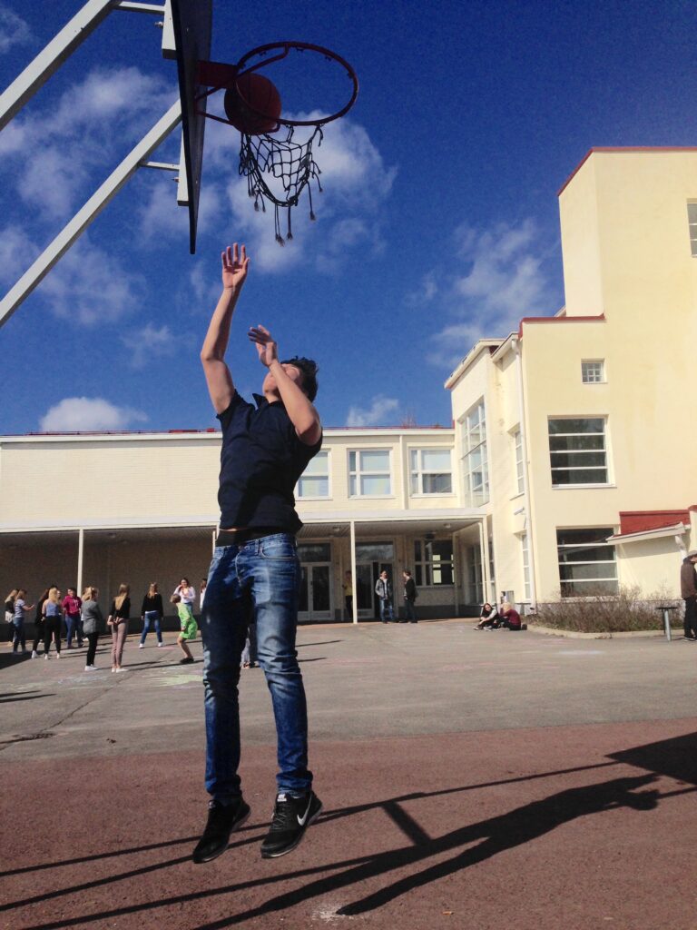 poika heittää koripalloa kesäisenä päivänä lukion pihalla